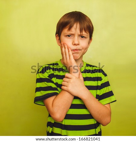 young boy child toothache pain in mouth, dental pain, holding his cheek on a green background