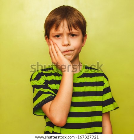 young kid boy child toothache pain in mouth, dental pain, holding his cheek on a green background