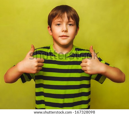 blonde boy kid in shirt holding thumbs up, showing sign yes emotion on a green background