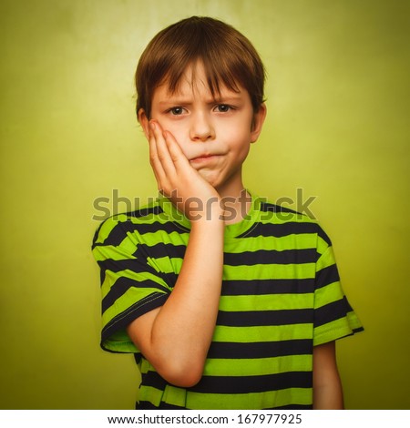 young kid boy child toothache pain in mouth, dental pain, holding his cheek on a green background gray