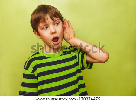 baby teenager boy listens to put a hand to his ear on a green background