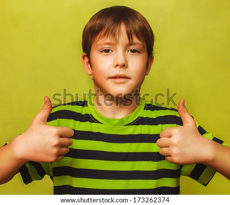 blonde boy kid in shirt holding thumbs up, showing sign yes emotion on a green background large