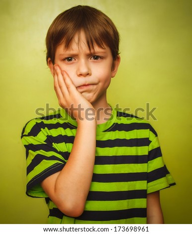 young kid boy child toothache pain in mouth, dental pain, holding his cheek on a green background gray large
