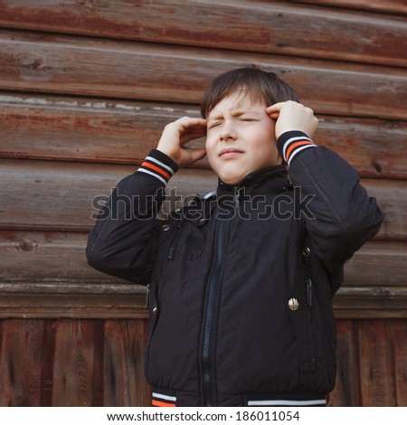 Teenage boy in jacket holding his head closed his eyes pain migraine disease on the background of wooden planks