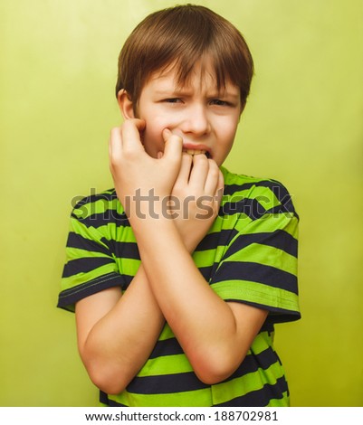 young kid child boy toothache pain in mouth, dental pain, holding his cheek on a green background
