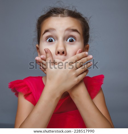 Teen brunette girl covering her mouth with her hands, experiencing a fright surprise bulging eyes portrait over gray background