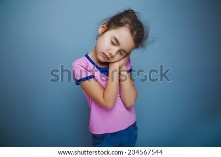 girl child wants to sleep hands under her cheek on a gray background