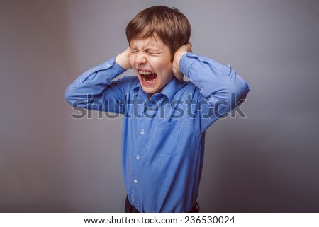 boy teenager yells covers his ears closed his eyes on a gray background