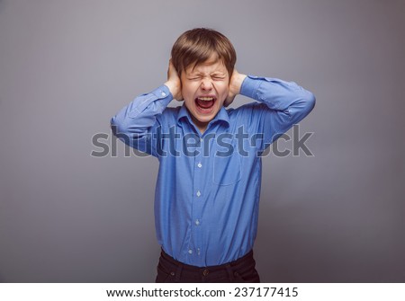 teenager boy covering his ears screaming hands on a gray background