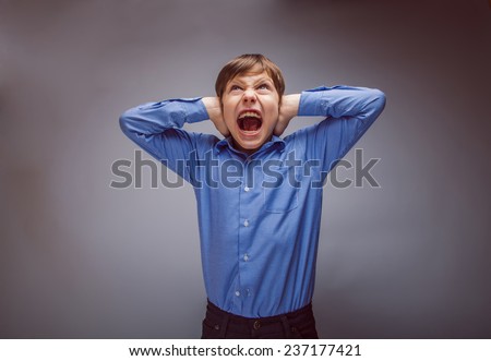 teenager boy shouts shut his ears opened his mouth on a gray background