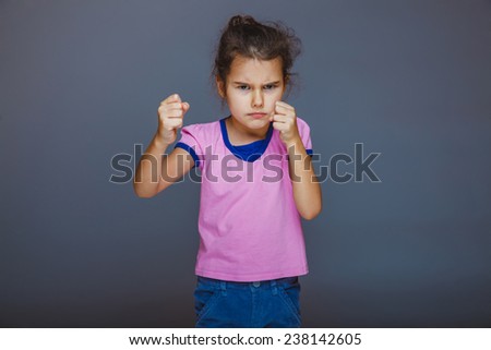 Teen girl shows angry fists on a gray background