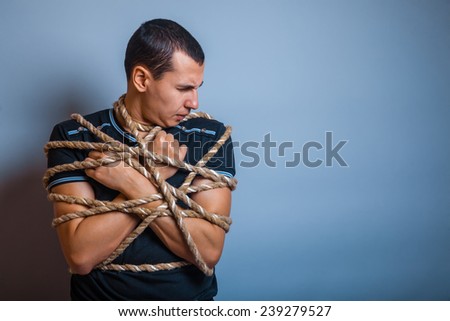 the man of European appearance brunet tied with rope on a gray background