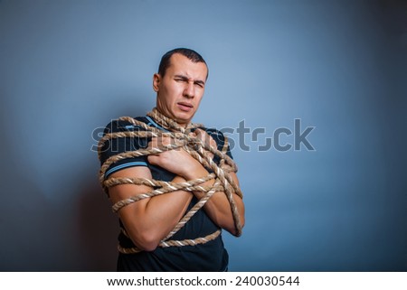30 years old man of European appearance tied with rope on a gray background