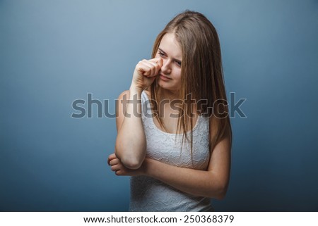 European-looking girl of twenty years crying, wiping tears by hand on a gray background