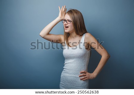 European appearance blonde girl with glasses put her hand to her head on a gray background, emotions