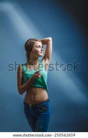 European appearance blonde girl threw her hands behind her head and lifted her shirt on a gray background, thoughtfulness