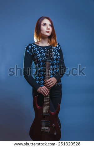 girl of European appearance holds a guitar in his hands on a gray background, sadness, longing, loneliness