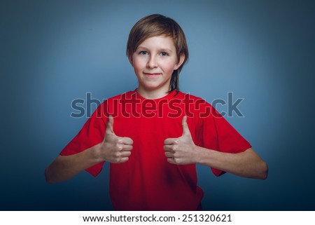 boy teenager European appearance in a red shirt showing sign yes on a gray background, joy cross process