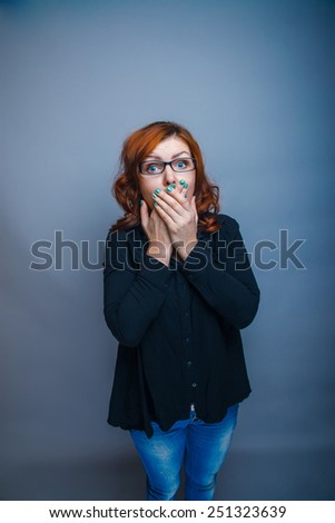 European-looking woman of thirty years covers mouth with her hands, surprised on a gray background