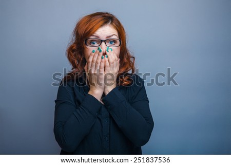 European-looking woman of thirty  years  covers  mouth with  her  hands,  surprised on a gray background