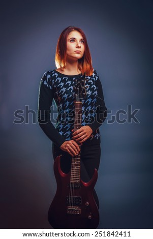 girl of European appearance holds a guitar in his hands on a gray background, sadness, longing, loneliness retro