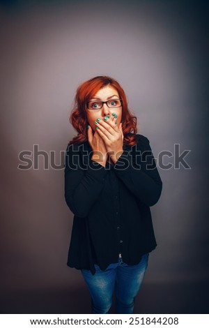 European-looking woman of thirty years covers mouth with her hands, surprised on a gray background retro