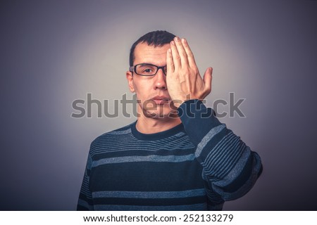 male of European appearance brunet in sweater covered half of his face with his hand on a gray background, mystery retro