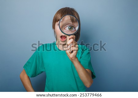 European-looking boy of ten years a joke, looking through a magnifying glass, large eyes, open mouth on a gray background