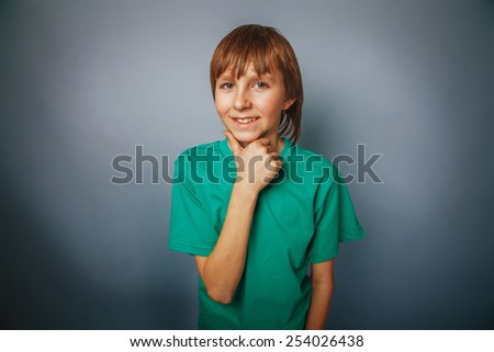 European-looking boy of ten years thinks hand at chin, smiling over gray background cross process