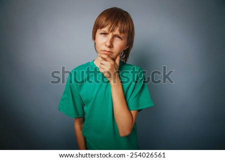 European-looking  boy of  ten  years thinking, hand under his chin on a gray background cross process