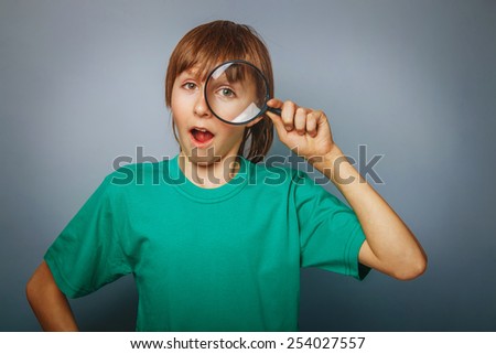 European-looking boy of ten years a  joke,  looking through a magnifying glass, a keen eye on gray background cross process