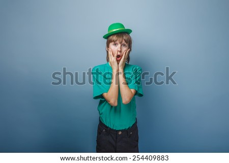 European appearance teenager boy in T-shirt with green hat put his hands to his face and wonders