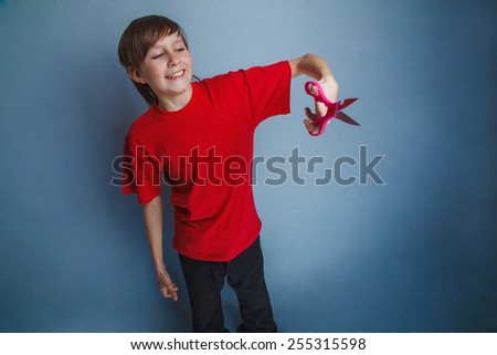 Boy, teenager twelve years in the red shirt red is holding of pair of scissors