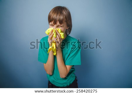 European-looking boy of ten years is ill, a handkerchief, a runny nose on a gray background