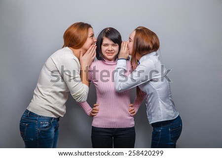 Three girls girlfriends talking in his ear, a secret on  a gray background