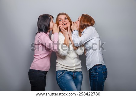 two girls European appearance blonde and brunette whispered in his ear the third the secret girl on a gray background, emotions