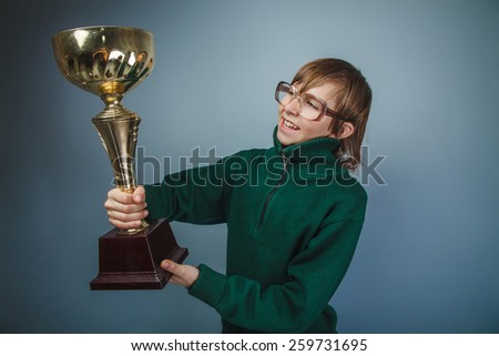 European-looking boy of ten years in glasses holding a cup in his hand, the reward on a gray background