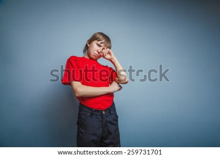 Boy, teenager, twelve years red in T-shirt, hand wipes tears, sadness