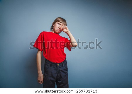 Boy, teenager, twelve years in  red T-shirt, hand wipes tears, sadness
