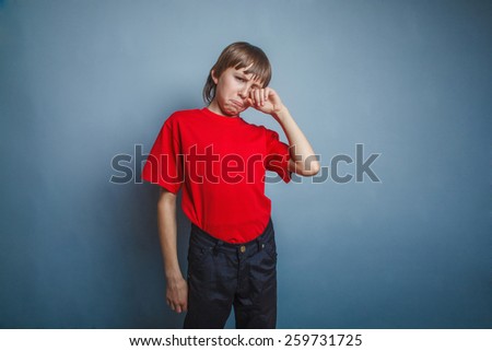 Boy, teenager, twelve years in the red T-shirt, hand wipes tears, sadness