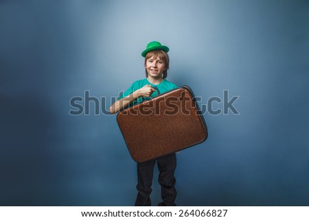 European-looking boy of  ten years in a hat holding a suitcase in hand, itinerary on a blue background