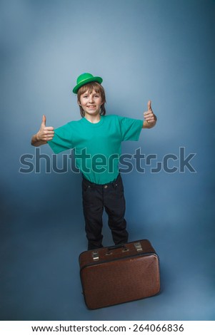 European-looking boy of  ten years in  a hat holding a suitcase in hand, itinerary on a blue background