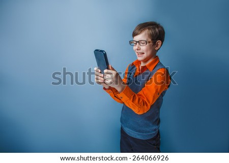 European-looking  boy of ten years in glasses holding tablet in hand, plays, pleasure on a blue background
