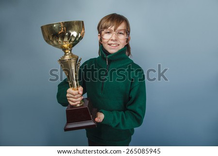 European-looking boy of ten years in glasses  holding a cup in  his  hand, the reward on a  gray background