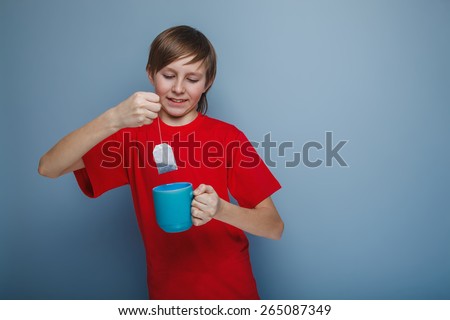 boy teenager European appearance in a red shirt brown drops tea bag in a cup on a gray background, tea