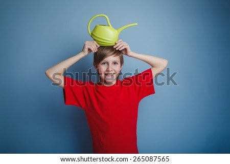 boy teenager European appearance in a red shirt brown hair watering can put on his head on a gray background