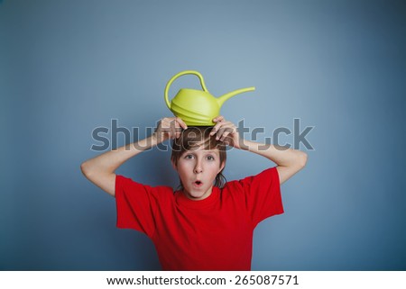 boy teenager European appearance in a red shirt brown hair watering can put on his head sticking her hands on a gray background, open mouth