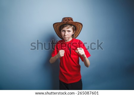 boy teenager European appearance in a red shirt brown hat clenched his fists on a gray background, the protection of