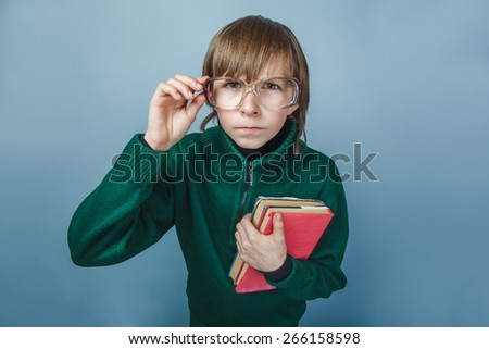 European-looking boy of ten years in glasses  with a book  showing thumb  up on a gray  background