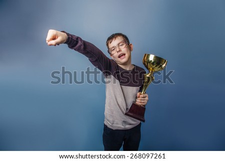 European-looking boy of ten years in glasses holding  a cup in his hand, the reward  on a gray background